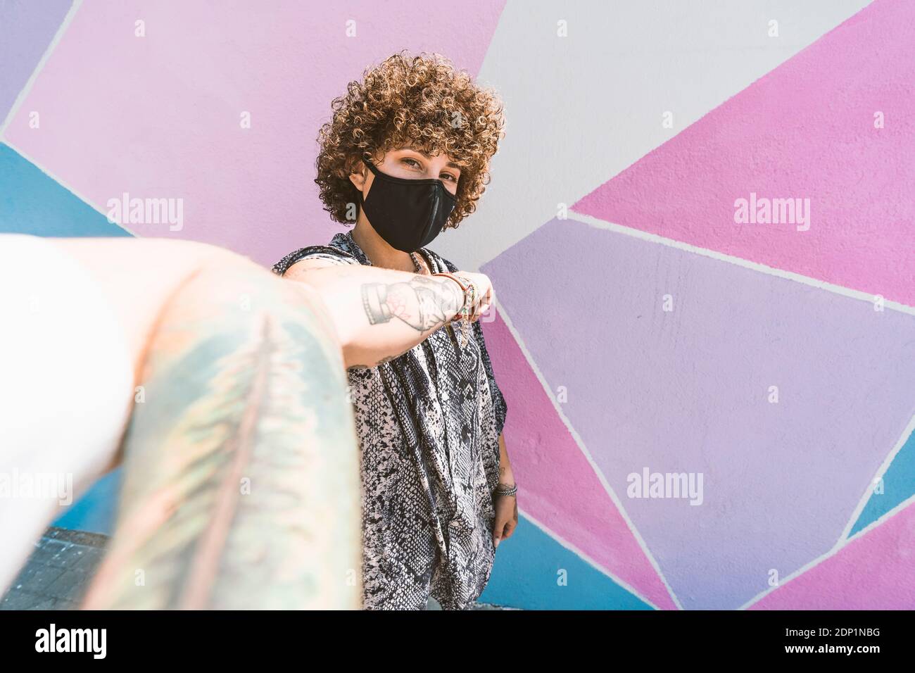 Joven hombre y mujer saludando con el codo topetón mientras está de pie contra la pared multicolor Foto de stock