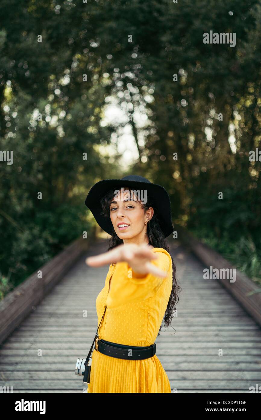 Mujer joven vistiendo un traje amarillo y sombrero negro con una cámara analógica a una cámara en mano boardwalk de madera Foto de stock