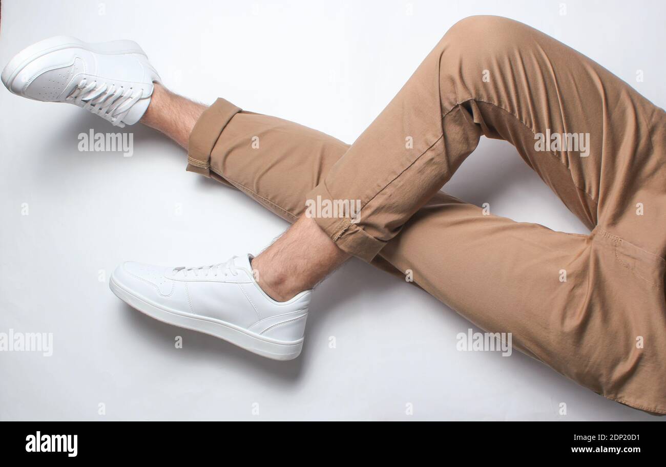 Un fragmento de patas masculinas en pantalones beige y zapatillas blancas  se asienta sobre un fondo blanco. Vista superior. Relajación Fotografía de  stock - Alamy