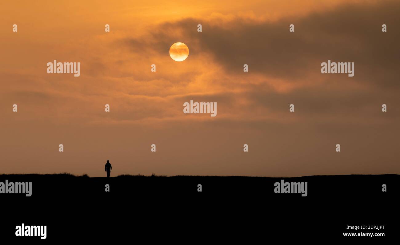 Persona solitaria caminando hacia la puesta de sol, Cumbria, Reino Unido. Foto de stock