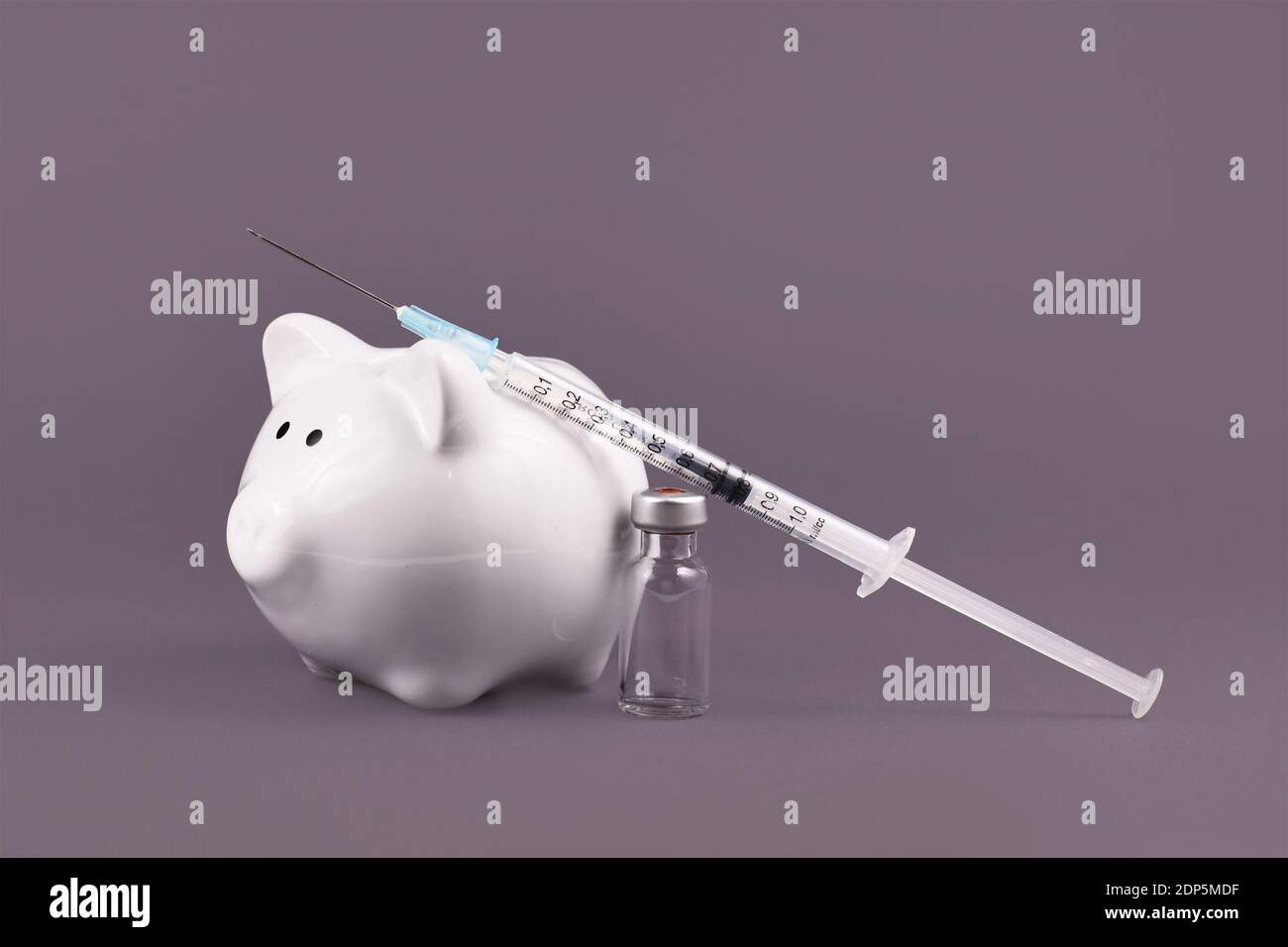 Concepto de costos de vacunación contra el virus de la corona con jeringa, vial de vacuna y banco piggy sobre fondo gris Foto de stock