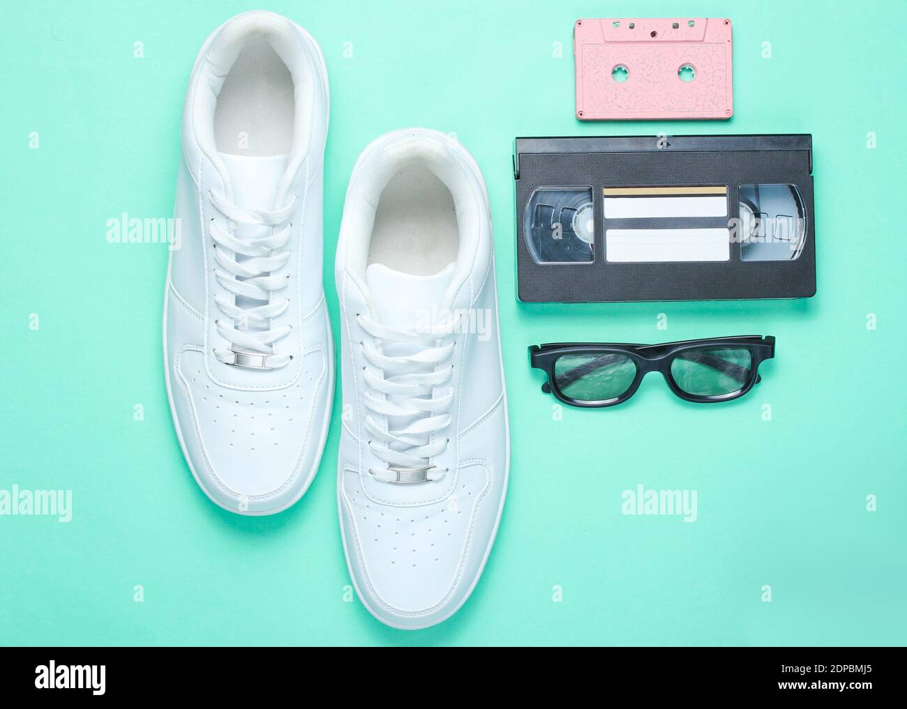 años 80, estilo retro. Zapatillas de lona blancas de cintura baja, casete de audio y vídeo, gafas 3D sobre un fondo de papel de color menta. Vista superior Foto de stock