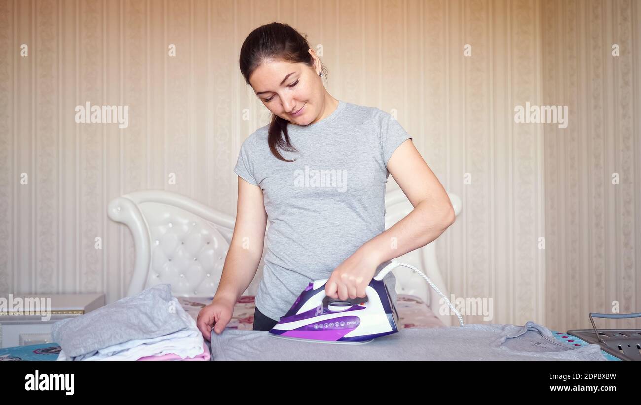 Mujer joven con pelo oscuro usando camisa gris hierros ropa después de  lavar con la moderna plancha púrpura y tabla de planchar en inicio cerrar  vista Fotografía de stock - Alamy