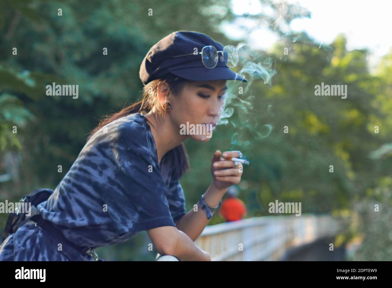 Mujer joven Fumando Cigarrillo contra los árboles Foto de stock