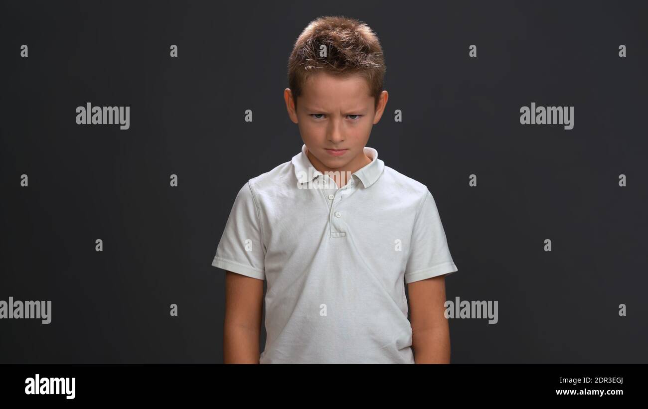 Un chico malvado mirando la cámara usando un polo blanco camisa y pantalones negros aislados sobre fondo negro Foto de stock