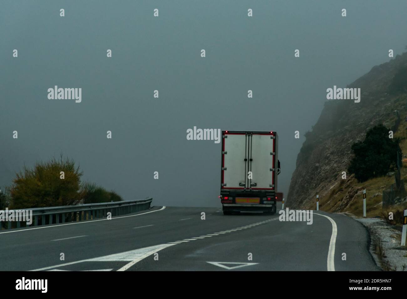 Camión con semirremolque refrigerado conduciendo por una carretera en un día foggy. Foto de stock