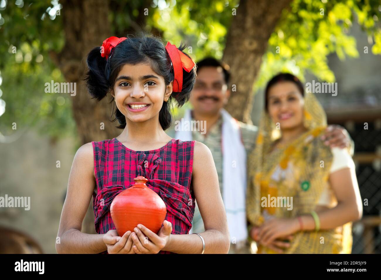 Familia India rural con hija sorprendida sosteniendo banco de piggy Foto de stock