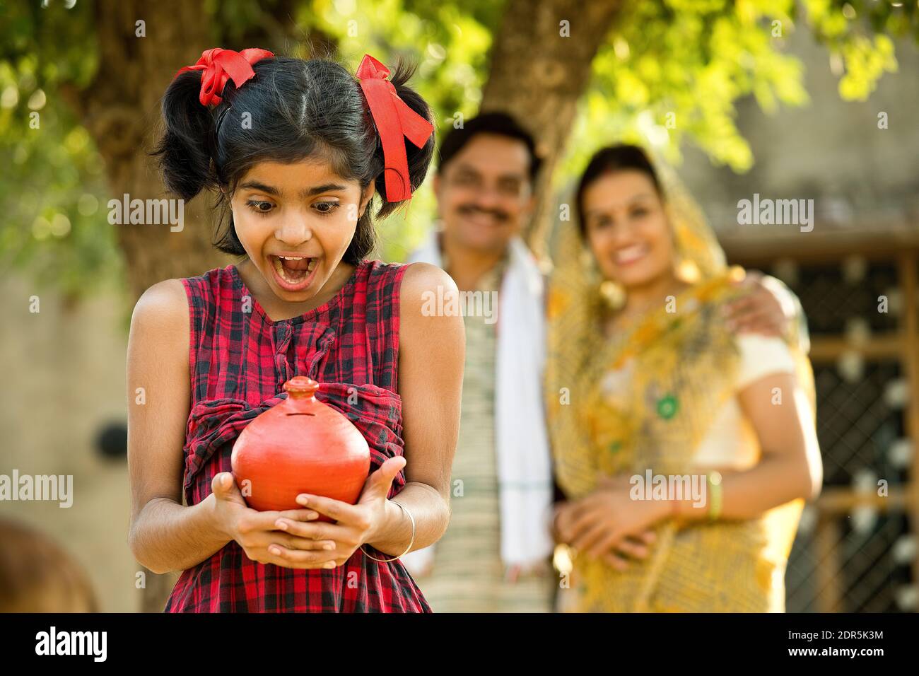 Familia India rural con hija sorprendida sosteniendo banco de piggy Foto de stock