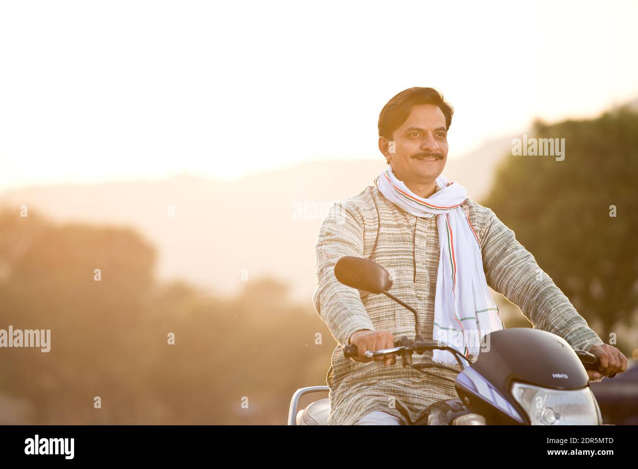 Feliz hombre rural indio que monta en motocicleta en el pueblo Foto de stock