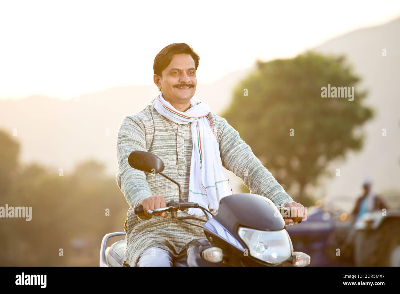 Feliz hombre rural indio que monta en motocicleta en el pueblo Foto de stock