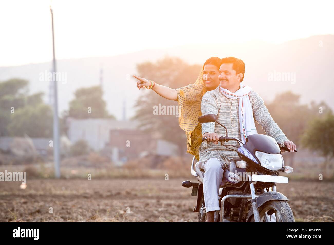 Feliz pareja rural de la India montando en motocicleta en el pueblo Foto de stock