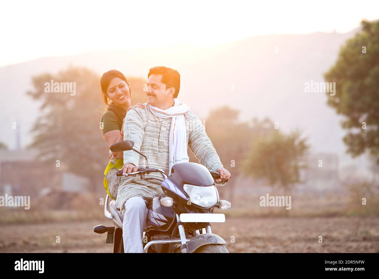 Feliz pareja rural de la India montando en motocicleta en el pueblo Foto de stock