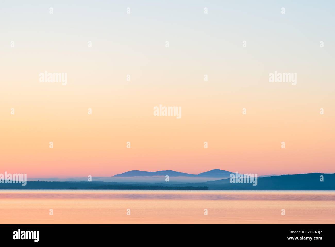 Vistas panorámicas del mar contra las montañas y el cielo despejado durante la puesta de sol Foto de stock