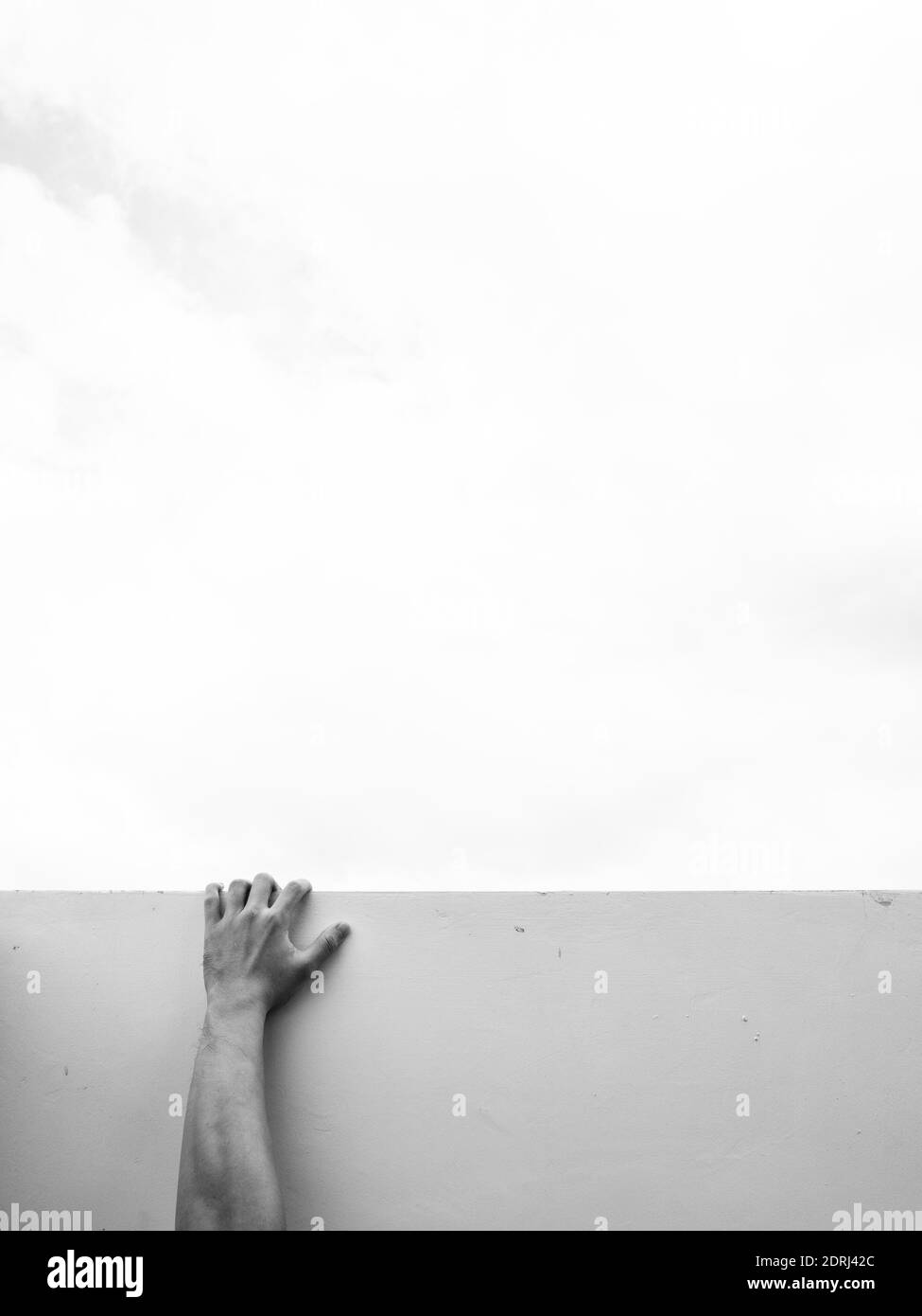 Mano humana sujetándose a la pared blanca contra un cielo gris que seña las luchas de la vida y colgando encendido Foto de stock