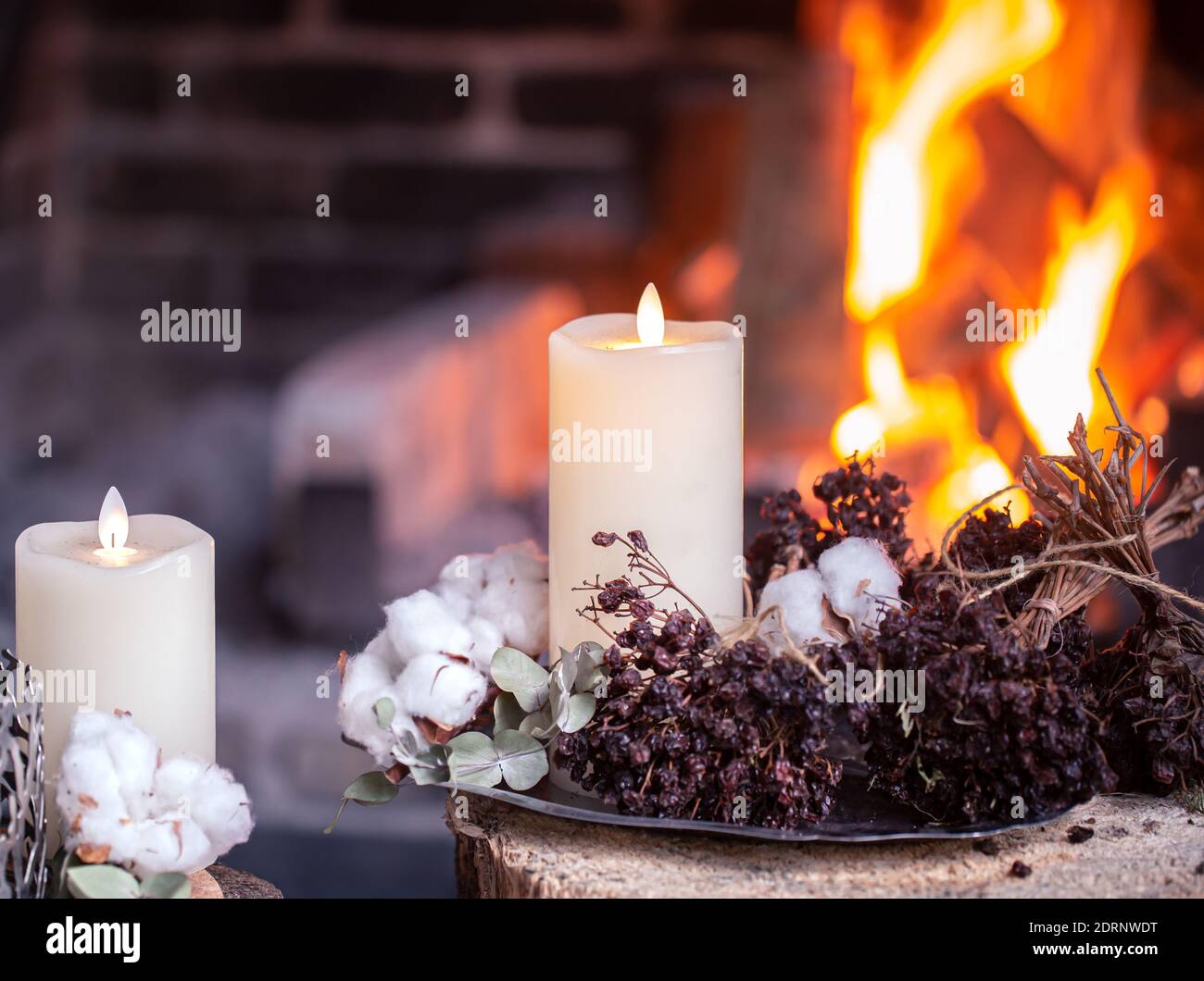 Hermosas velas decoradas con flores secas y algodón están ardiendo cerca de  la chimenea. El concepto de unas vacaciones acogedoras Fotografía de stock  - Alamy