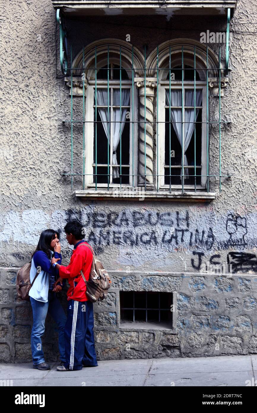 Joven pareja de pie junto a la pared con Bush fuera de América Latina / Fuente Bush de América Latina graffiti, la Paz, Bolivia Foto de stock