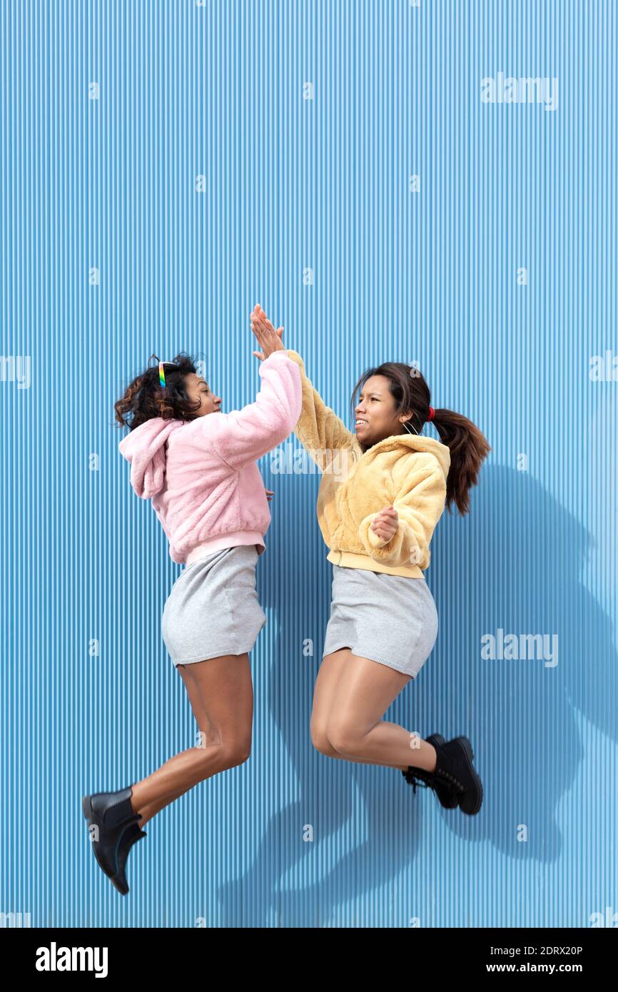 Dos chicas amistosas saltando y golpeando sus manos en el aire sobre un  fondo azul. Espacio para texto. Concepto de amistad Fotografía de stock -  Alamy