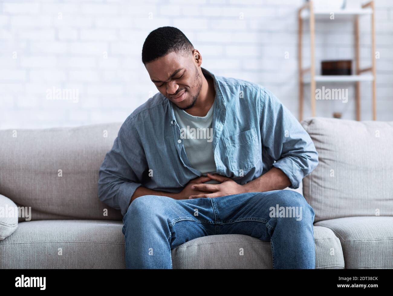 Black Guy teniendo dolor de estómago doloroso tocar dolor de estómago sentado en el interior Foto de stock