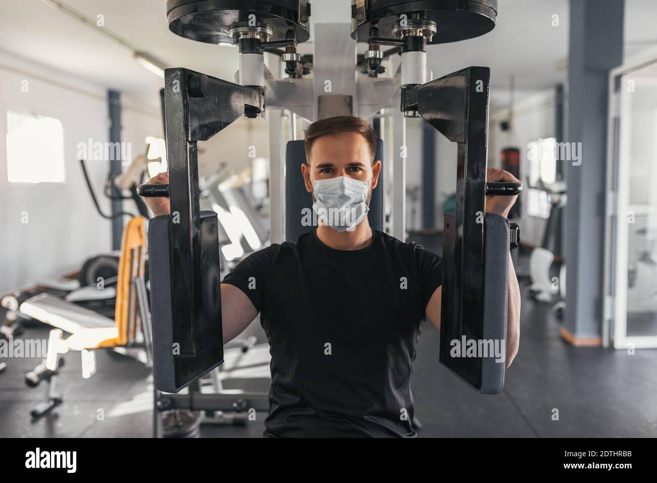 Foto Joven hombre hispano en forma en el gimnasio que va a hacer ejercicio  en la máquina de fitness, flexiona los músculos. Culturista preparado para  entrenar, va a hacer press de hombros. –
