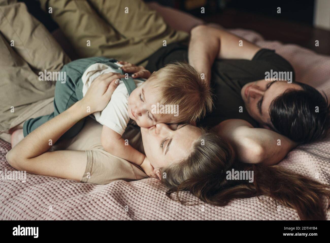 Feliz familia con un pequeño hijo acostado y jugando en la cama en casa Foto de stock