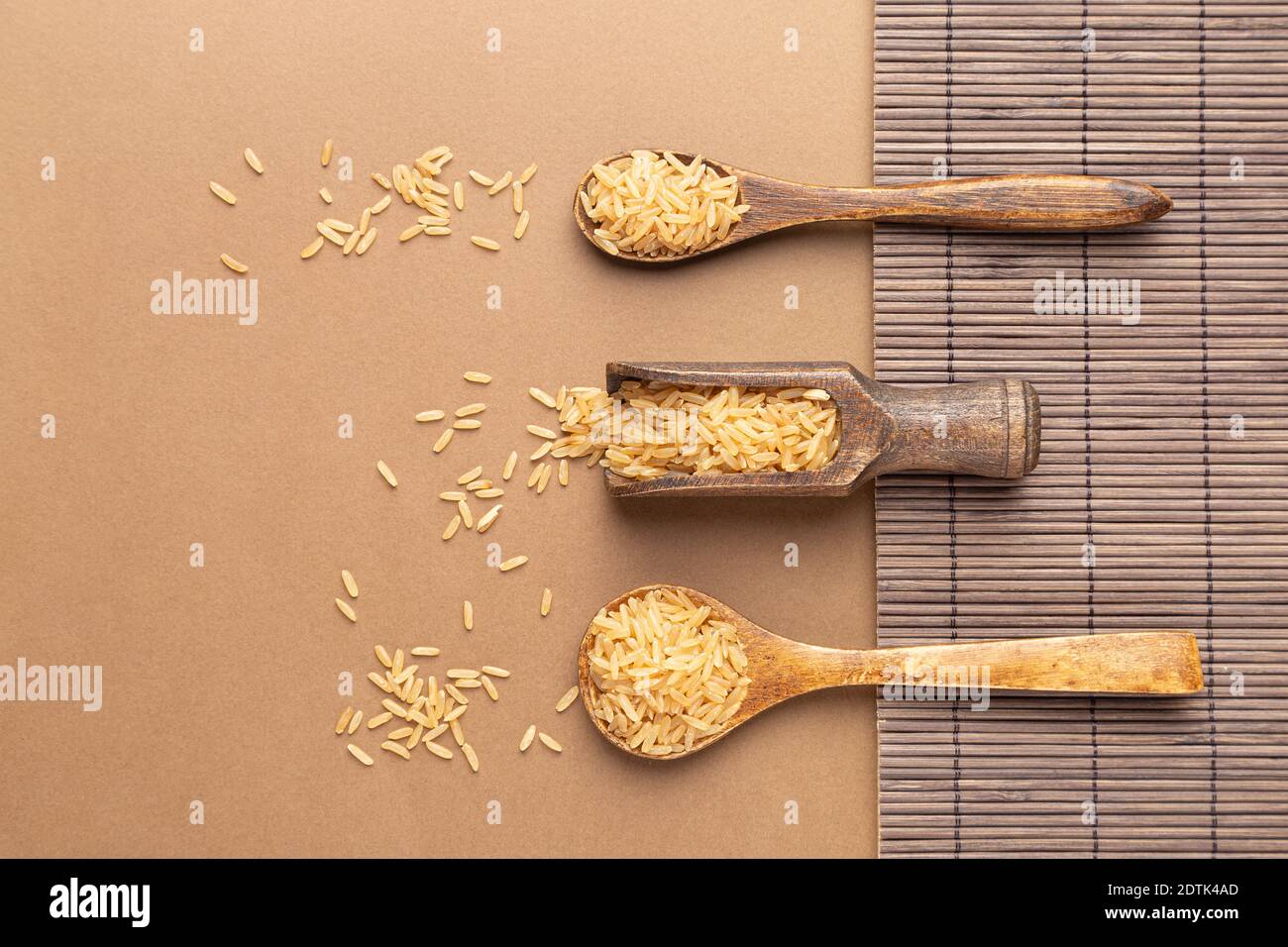 Cucharas con arroz marrón sobre una base marrón y de madera. Lay plano. Foto de stock