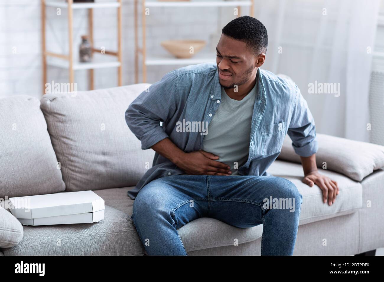 Un chico afroamericano que tiene dolor de estómago después de comer pizza en casa Foto de stock
