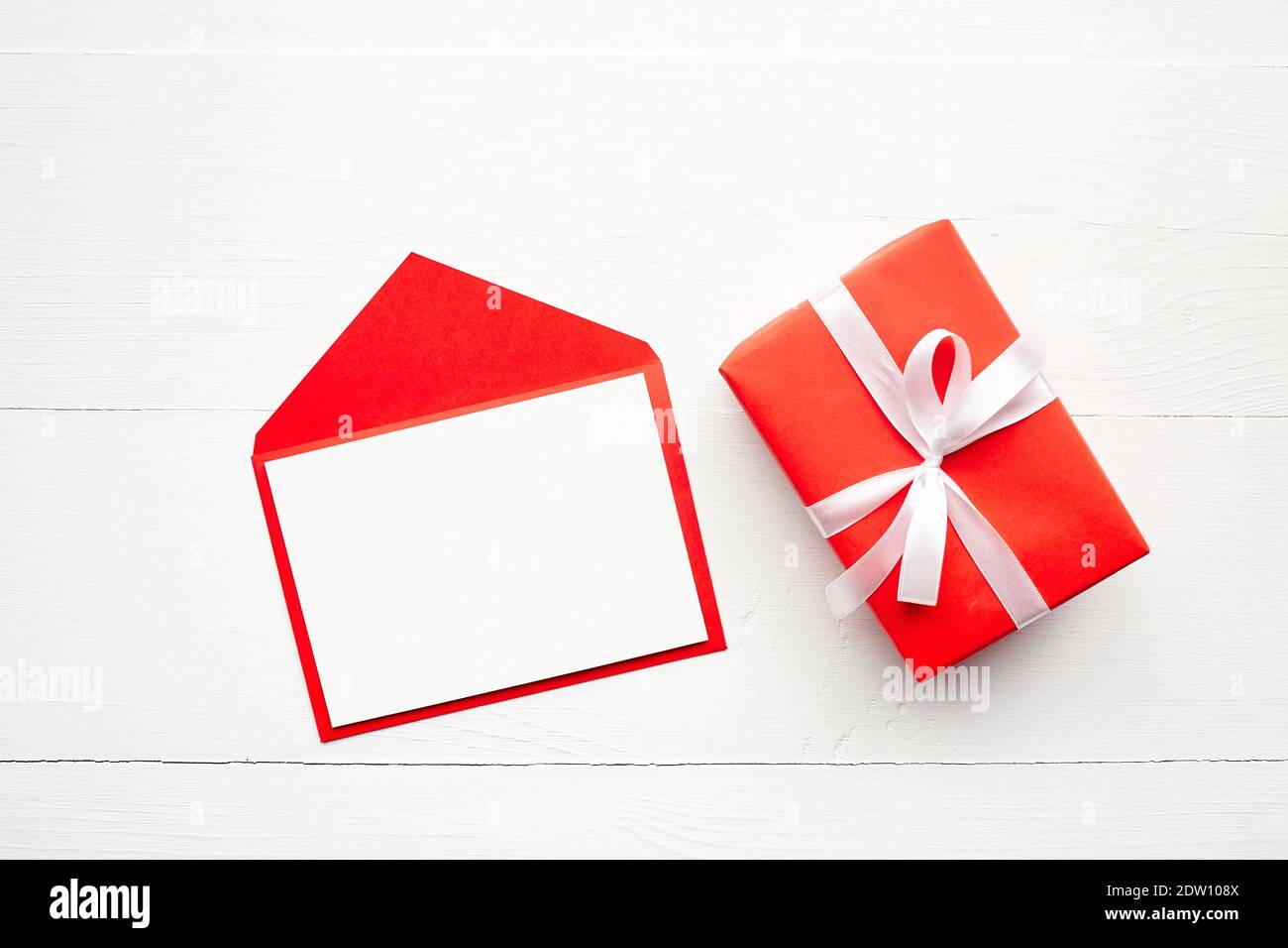Tarjeta de felicitación mockup, tarjeta blanca con sobre de papel, caja de  regalo con cinta sobre fondo de mesa de madera. Tarjeta de felicitación de  San Valentín, llay plano Fotografía de stock -