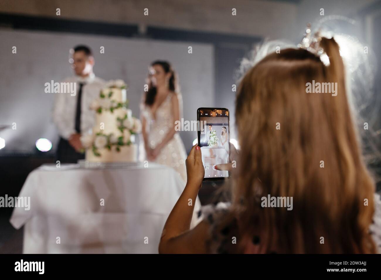 Niña tomando una foto de recién casados y pastel en el smartphone. Lugar para el texto. Fondo de la boda Foto de stock