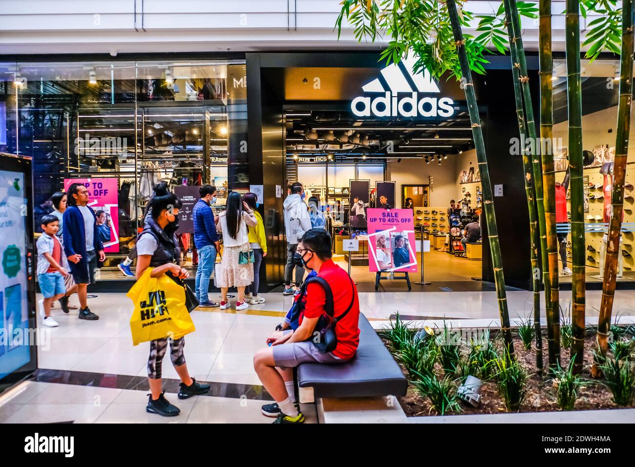 Melbourne, Australia. 23 de diciembre de 2020. Un hombre sentado fuera  mientras otros se alinean en la tienda Adidas durante las compras navideñas  en el centro comercial Chadstone - la capital de