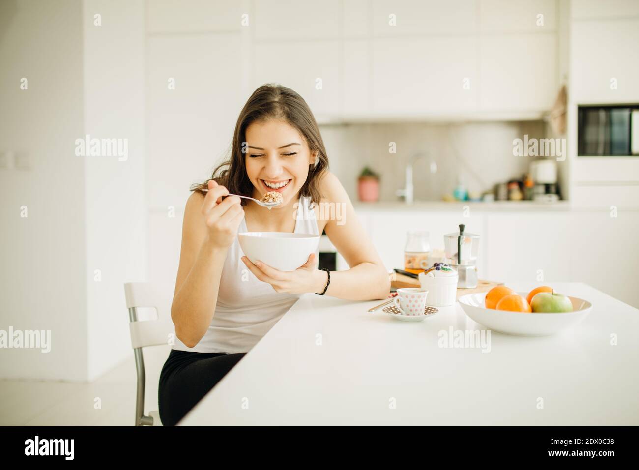 Joven mujer sonriente comiendo cereal.Desayuno saludable.comenzando su día.dieta,fitness y salud mental Care.energía positiva y emoción.productividad,h Foto de stock
