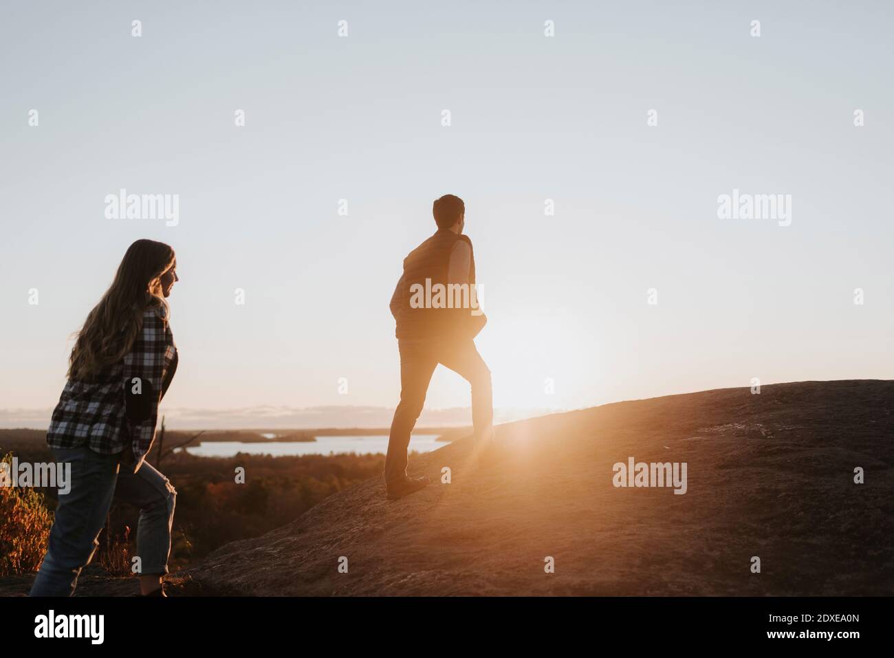 Una pareja joven caminando cuesta arriba contra poner el sol Foto de stock
