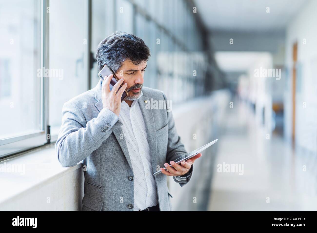 Profesor masculino hablando en el teléfono móvil mientras mira digital  tablilla contra ventana en el corredor universitario Fotografía de stock -  Alamy