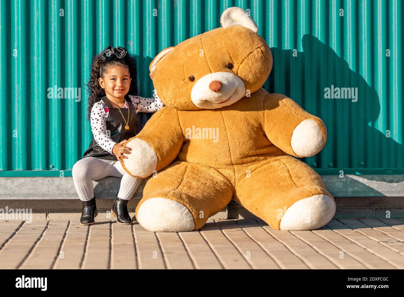 Chica sonriente sentada con un osito de peluche contra una pared verde Foto de stock