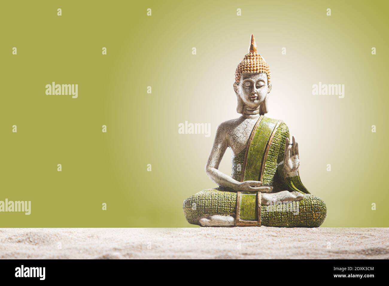 Estatua de Buda verde y dorada, sobre arena de fondo verde. Meditación, espiritualidad y concepto zen. Foto de stock