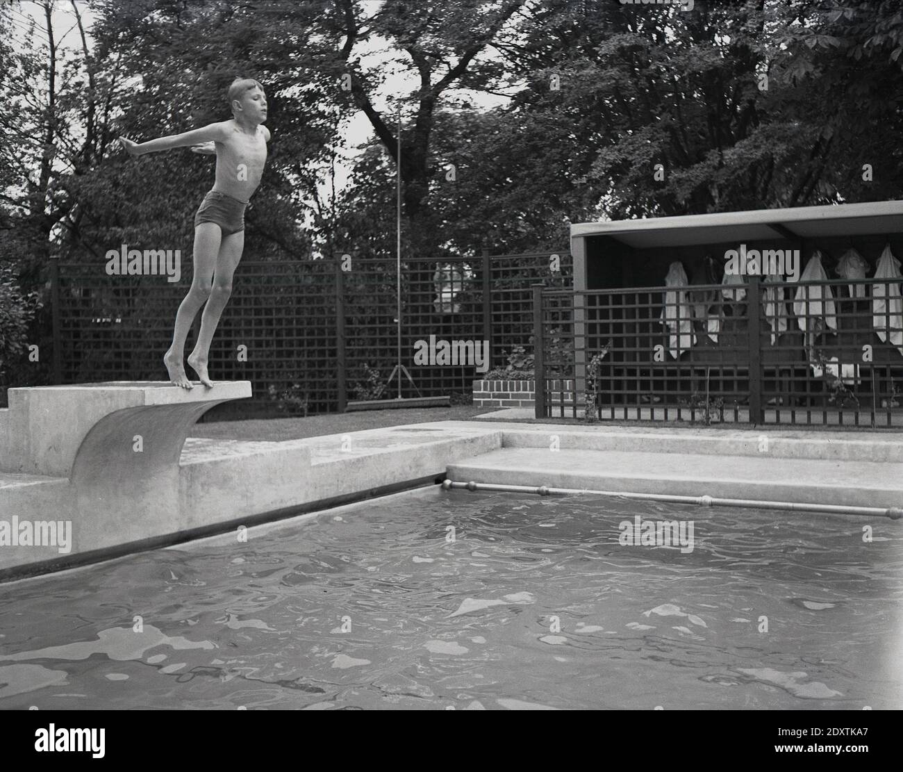 Años cincuenta, un niño histórico a punto de sumergirse en el agua desde una tabla de buceo de hormigón en una piscina al aire libre, Inglaterra, Reino Unido. Foto de stock