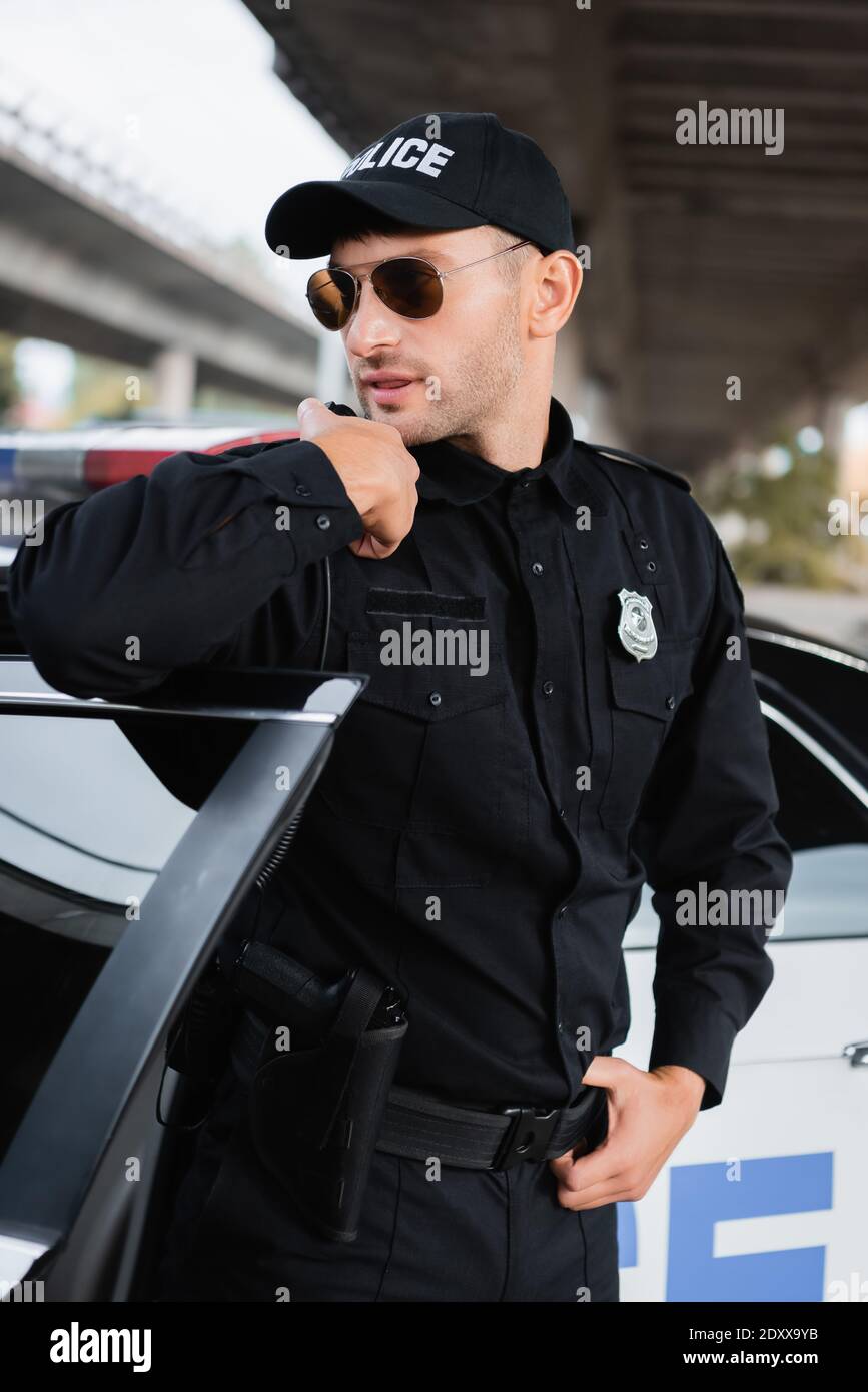 Polic a en gafas de sol usando walkie talkie cerca de coche en la