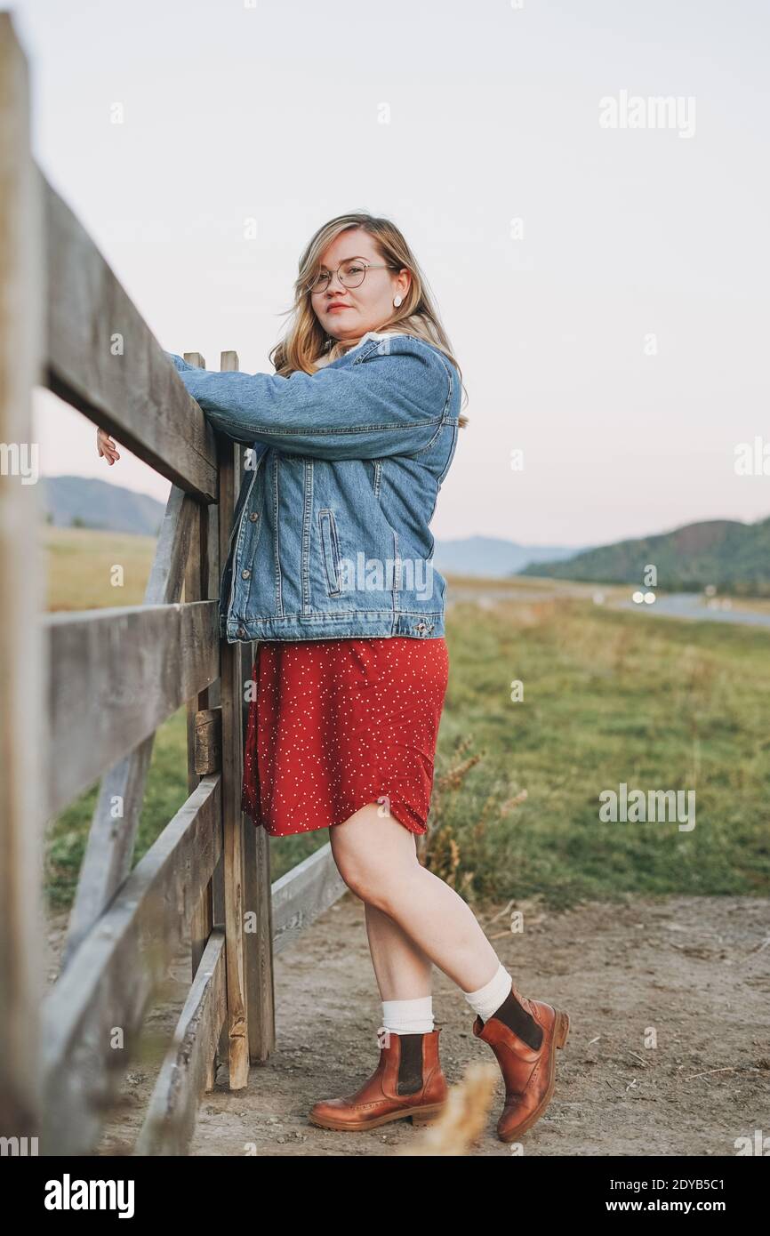 Joven mujer rubia con estilo en chaqueta de jeans y vestido rojo cerca de  la vieja cerda de madera en las montañas Fotografía de stock - Alamy