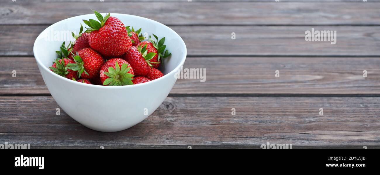 Fruta de fresas maduras en un tazón blanco sobre fondo de madera con espacio para copias. Concepto de alimentación saludable. Foto de stock