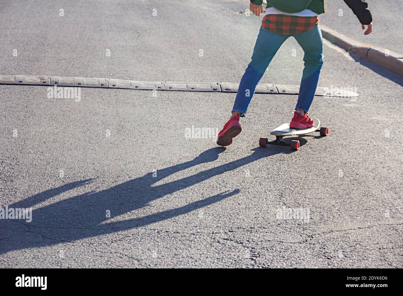 Vista de las piernas de un joven patinador en un monopatín acercándose al bache de velocidad en una calle de la ciudad Foto de stock