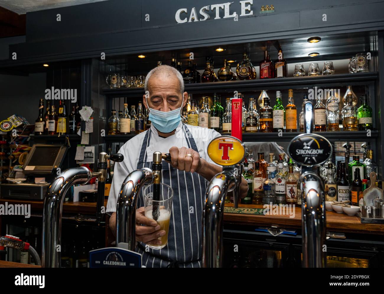 Barman usando delantal y máscara durante la pandemia Covid-19 verter pinta de cerveza de la bomba, Castle Inn, Dirleton, East Lothian, Escocia, Reino Unido Foto de stock