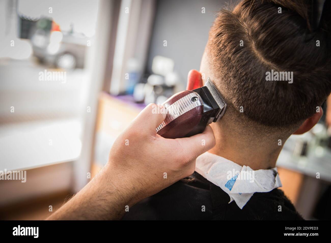 Primer plano de la mano de un barbero que está cortando el pelo a. un cliente en su casa de peluquero Foto de stock
