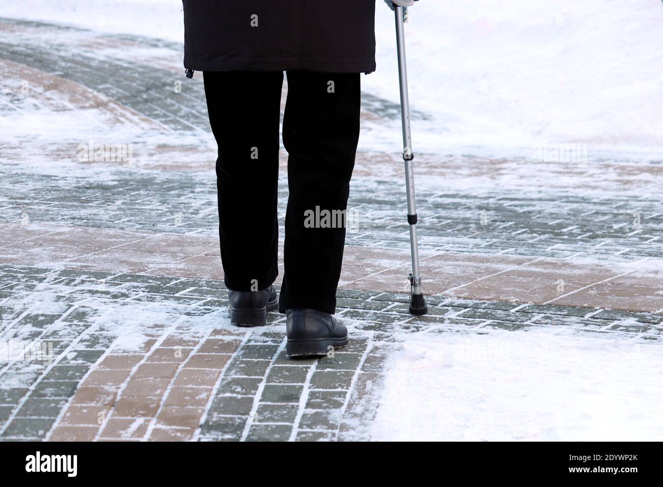 Anciano con bastón en una calle de invierno. Concepto de cojera, vejez, clima nevado Foto de stock