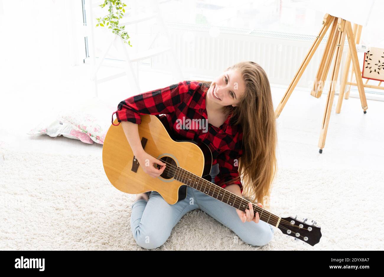 Chica linda con pelo largo y suelto tocando la guitarra en la luz habitación Foto de stock