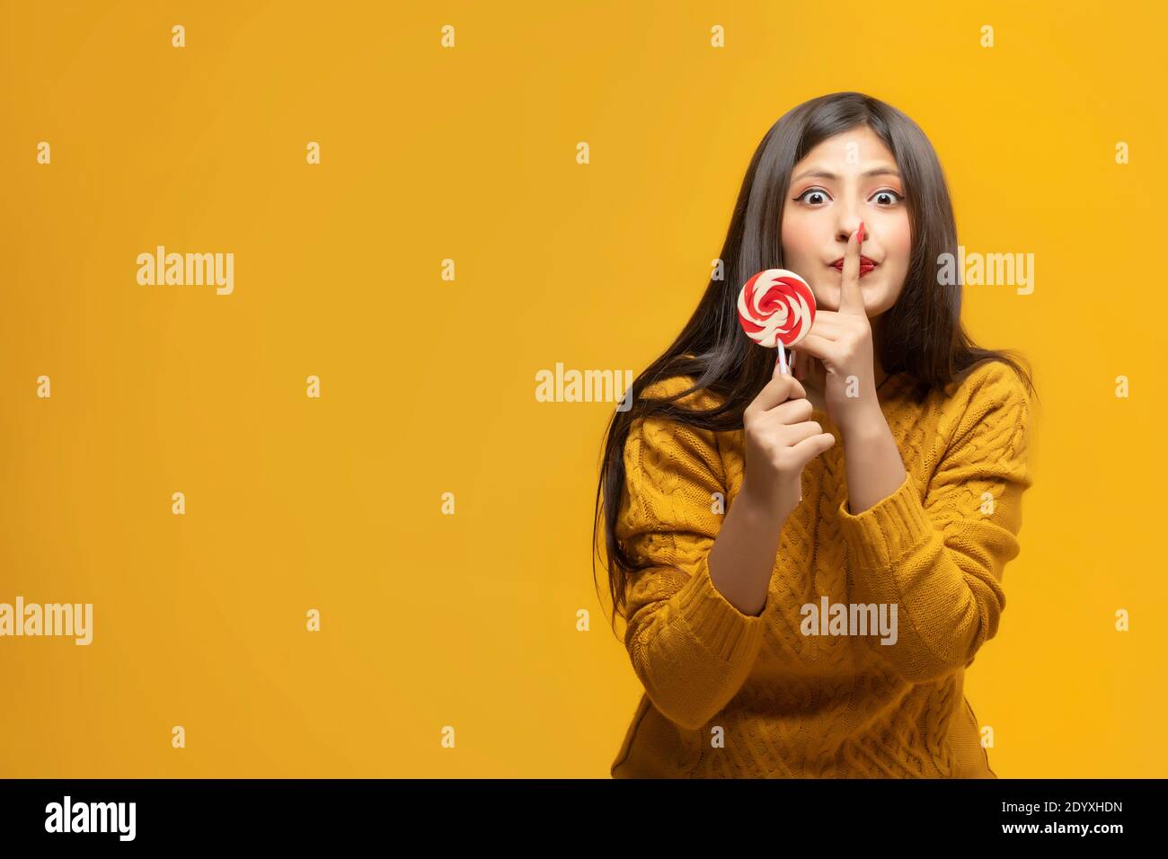 Retrato de una joven sosteniendo un lollipop con el dedo en los labios Foto de stock