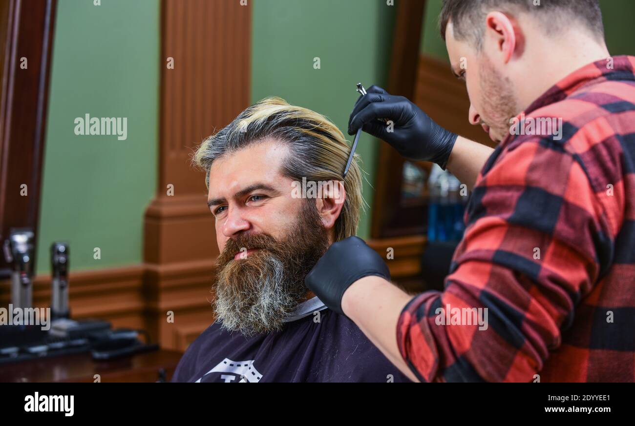 Hipster barbero hombre peluquero cortando el cabello y dando forma a la  barba de un hombre en un sillón
