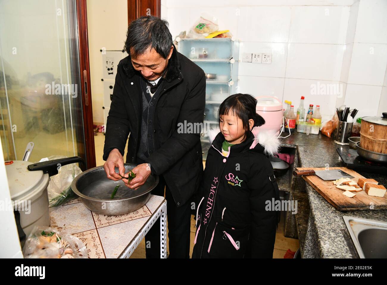 (201229) -- BIJIE, 29 de diciembre de 2020 (Xinhua) -- Li Changde y su nieta Li Qingyi permanecen en la cocina de su nueva casa en una comunidad recién construida para aliviar la pobreza en el antiguo municipio de Shexiang del condado de Dafang, al suroeste de la provincia de Guizhou, 23 de diciembre de 2020. Li Siyu, de 8 años, y su hermana Li Qingyi, de 6 años, vivían en la aldea de Hetou como miembros de un hogar asolado por la pobreza. Tenían que pasar casi una hora caminando a la escuela todos los días. Sus padres trabajaban en otras ciudades y Li Changde, el abuelo de 68 años, asumió la responsabilidad de llevarlos a y. Foto de stock