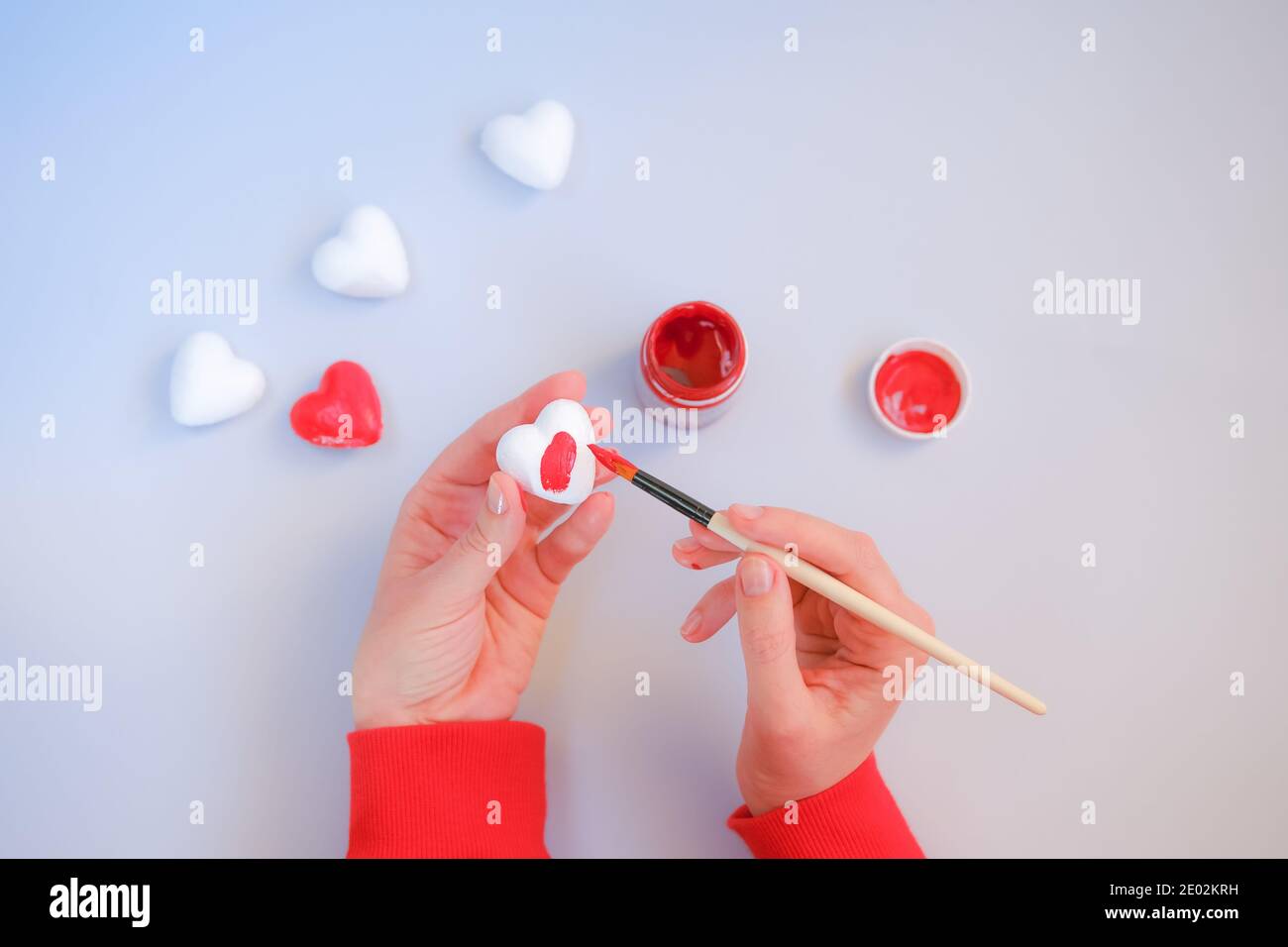 Las manos de la mujer pintan corazones decorativos en rojo. Preparación del día de San Valentín. Foto de stock