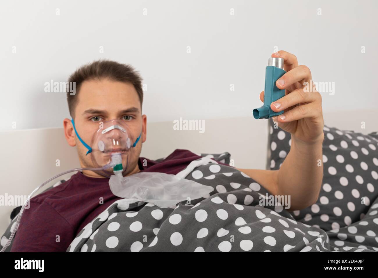 El paciente masculino con mascarilla de oxígeno en casa está acostado en la  cama, sosteniendo un inhalador con salbutamol Fotografía de stock - Alamy