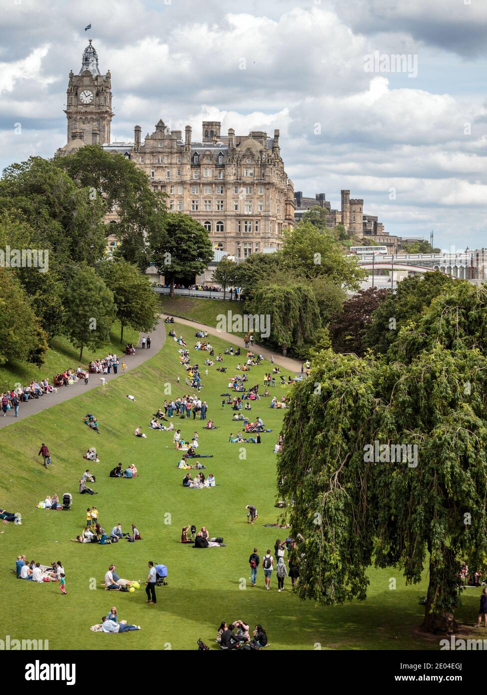 La gente disfruta del sol de verano en Princes Street Gardens en el centro de Edimburgo, con el Hotel Balmoral en el fondo. Foto de stock