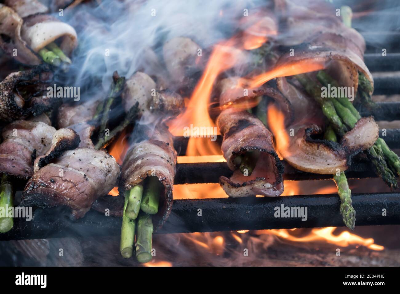 Espárragos de cocina de fuego abierto envueltos en tocino, con humo del fuego y llama abierta Foto de stock